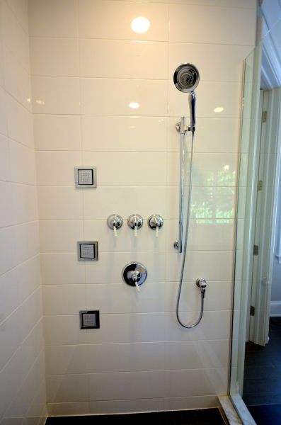A shower with a shower head and three square buttons on the wall.