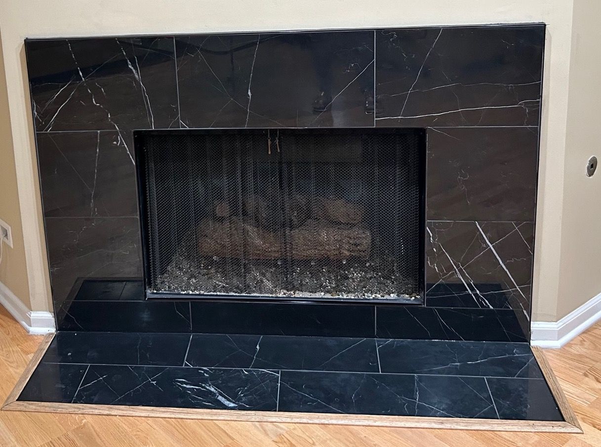 A fireplace with black tiles and a metal screen