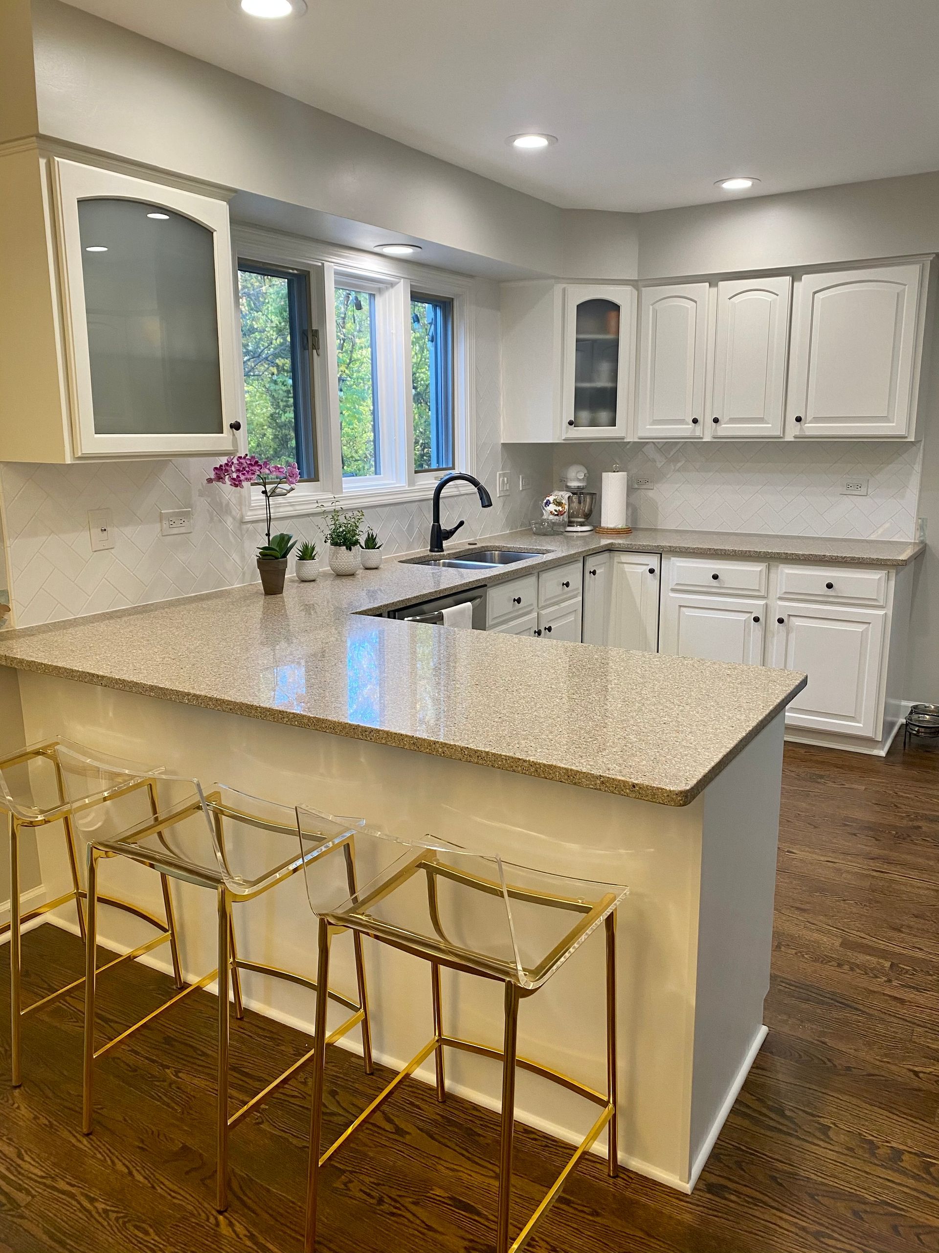 A kitchen with white cabinets , granite counter tops , and gold bar stools.