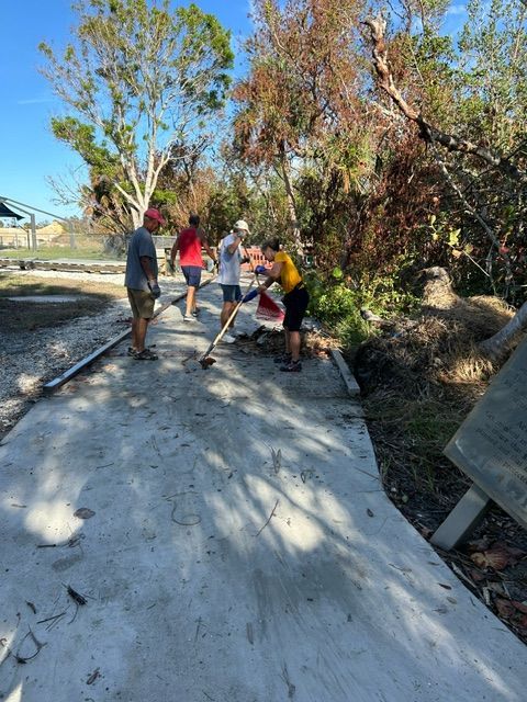 People working together to clear debris from a cracked path beside trees and bushes.