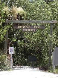 Wooden entrance sign reading “Matanzas Pass Preserve” amid dense green foliage