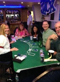 People seated around a green casino table, smiling and playing cards in a bar or lounge