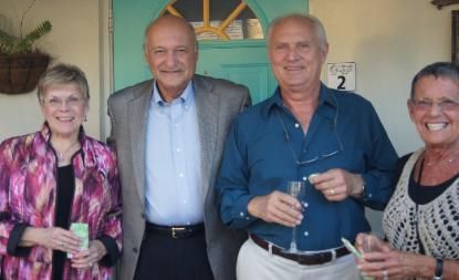 Four people smiling and posing indoors, holding drinks in front of a green door