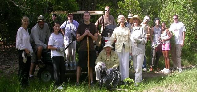 Group of people posing outdoors in a grassy garden, some holding walking sticks, with trees in the background
