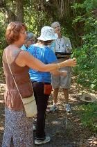 Three people outdoors in a wooded area, looking and pointing at something off-camera.
