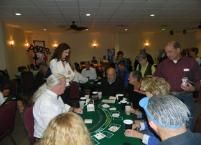 People gathered around a green casino table, watching a card game in a dimly lit room.