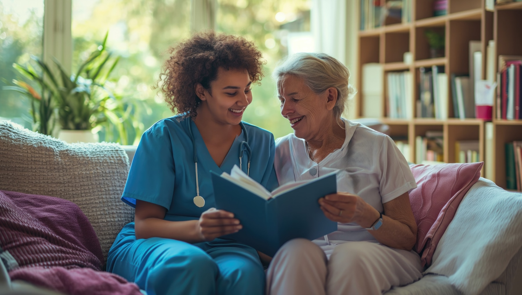 A nurse is reading a book to an elderly woman on a couch.