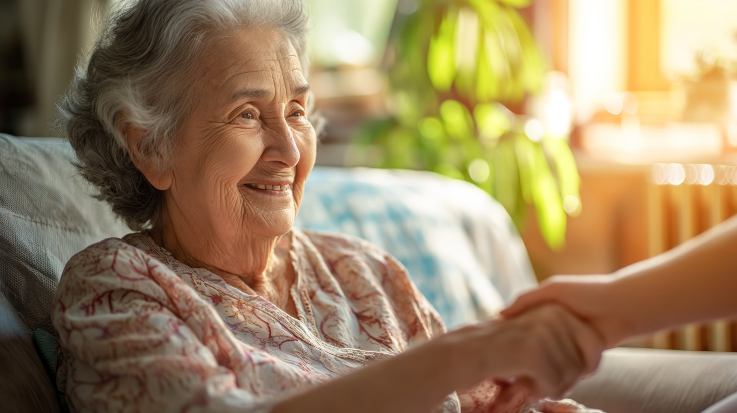 An elderly woman is sitting on a couch holding a woman 's hand.