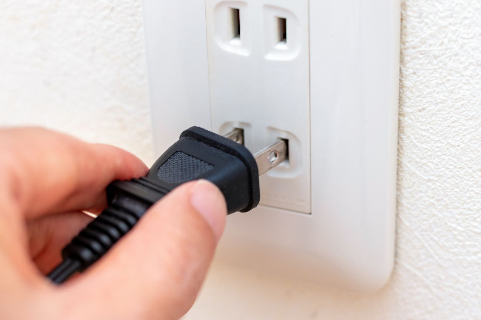 Hand plugging a black electrical cord into a white wall outlet