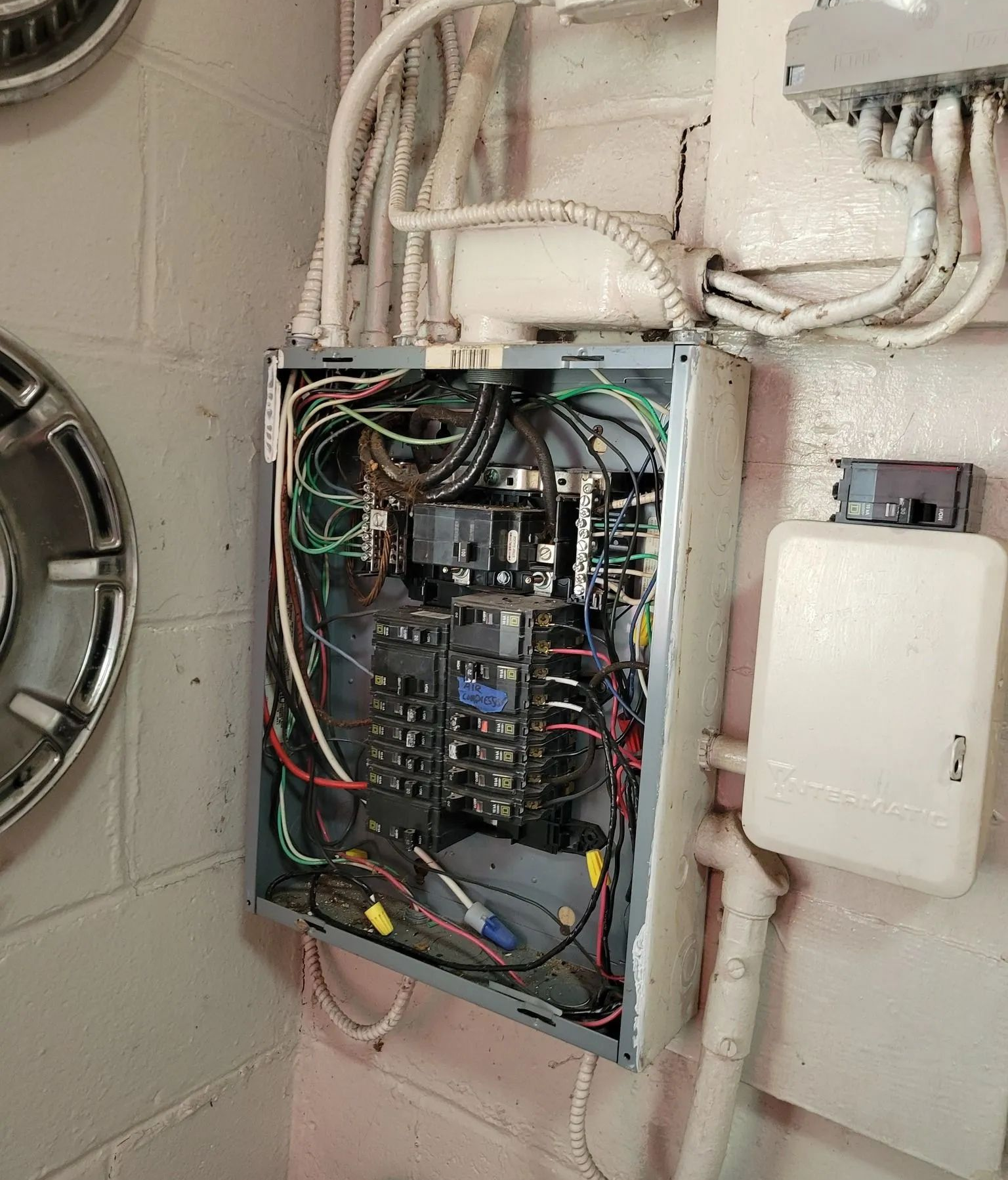 Open electrical panel with exposed wiring and breakers on a wall