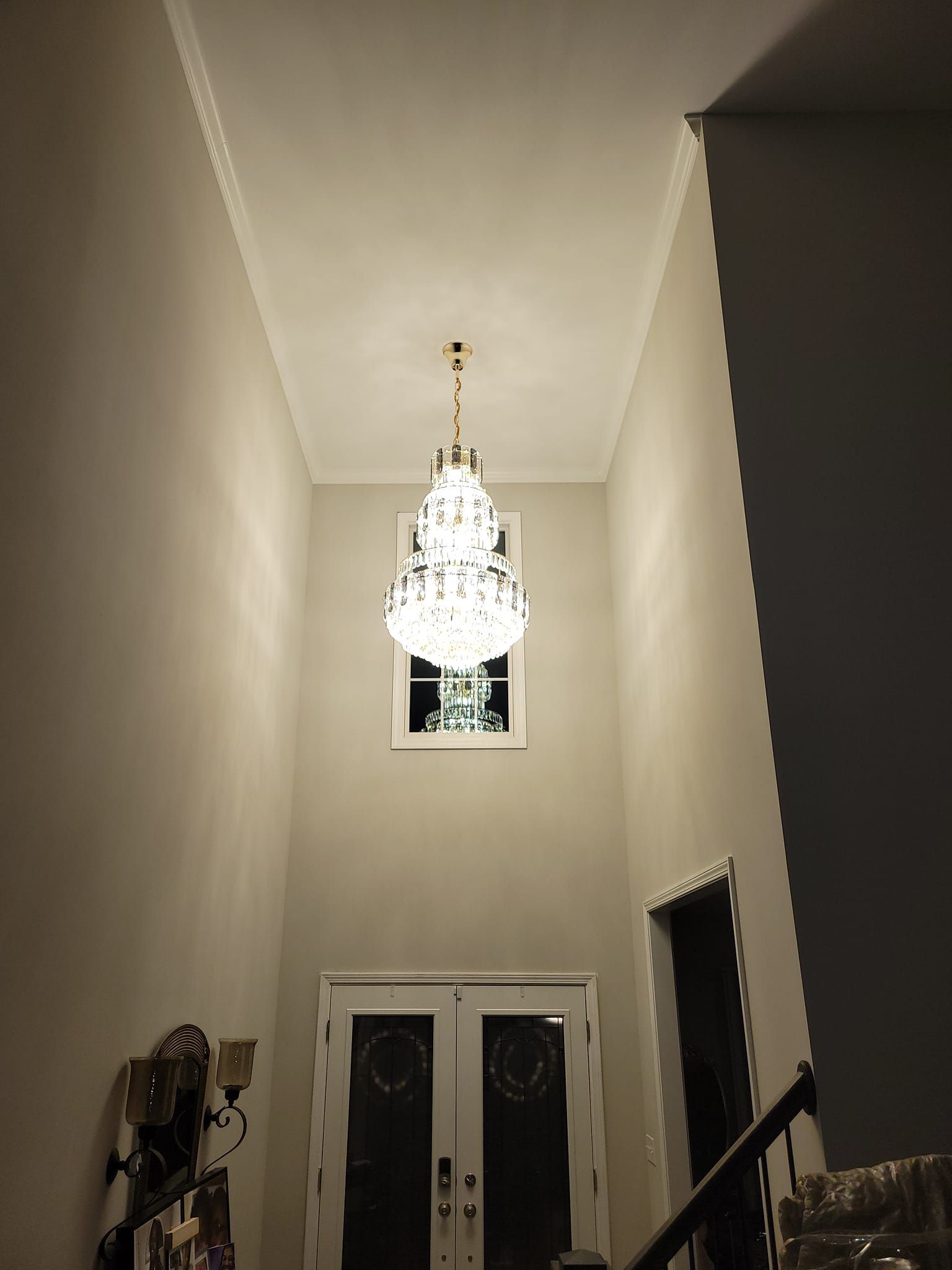 Chandelier hangs in a tall entryway with a double door at the bottom.