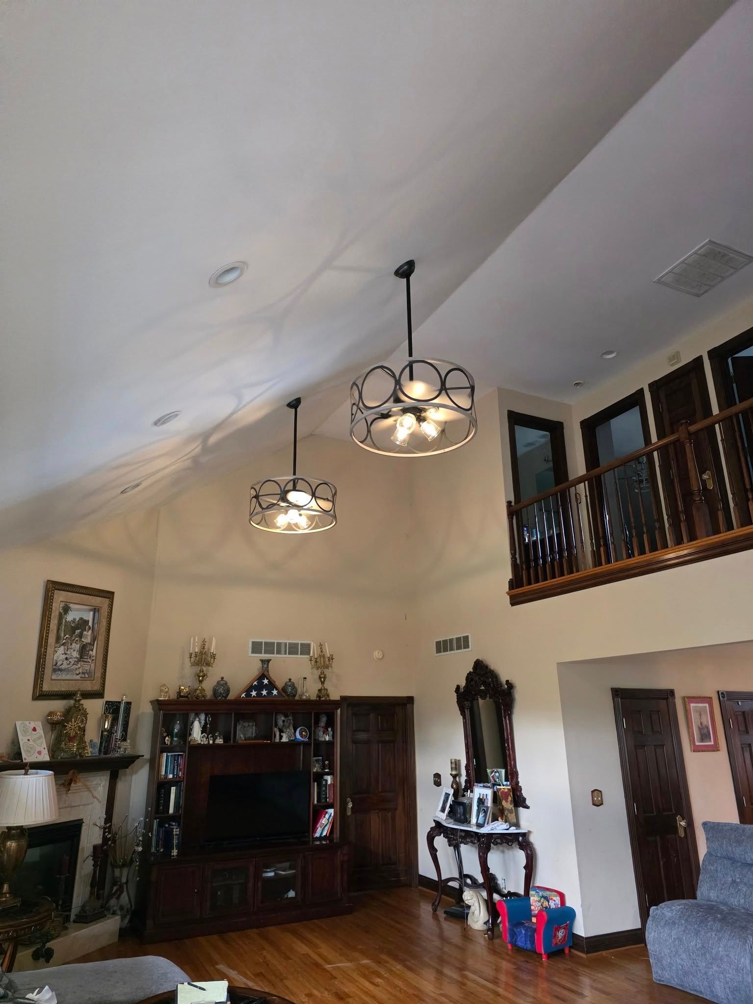 A living room with two hanging orb chandeliers, a television console, hardwood floors, and a balcony overlook.