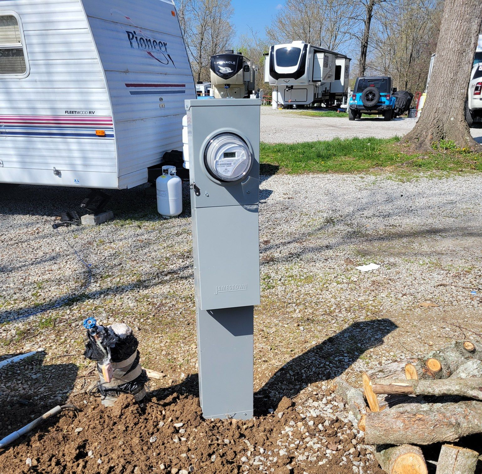 Gray electrical box with meter at a campsite, with RVs and a jeep in the background.