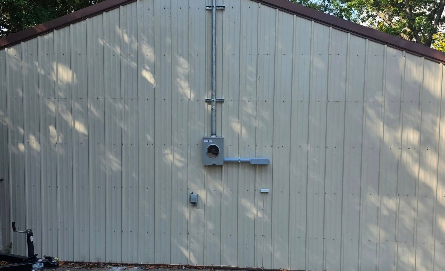 A gray electrical panel and conduit mounted on a light beige shed exterior.