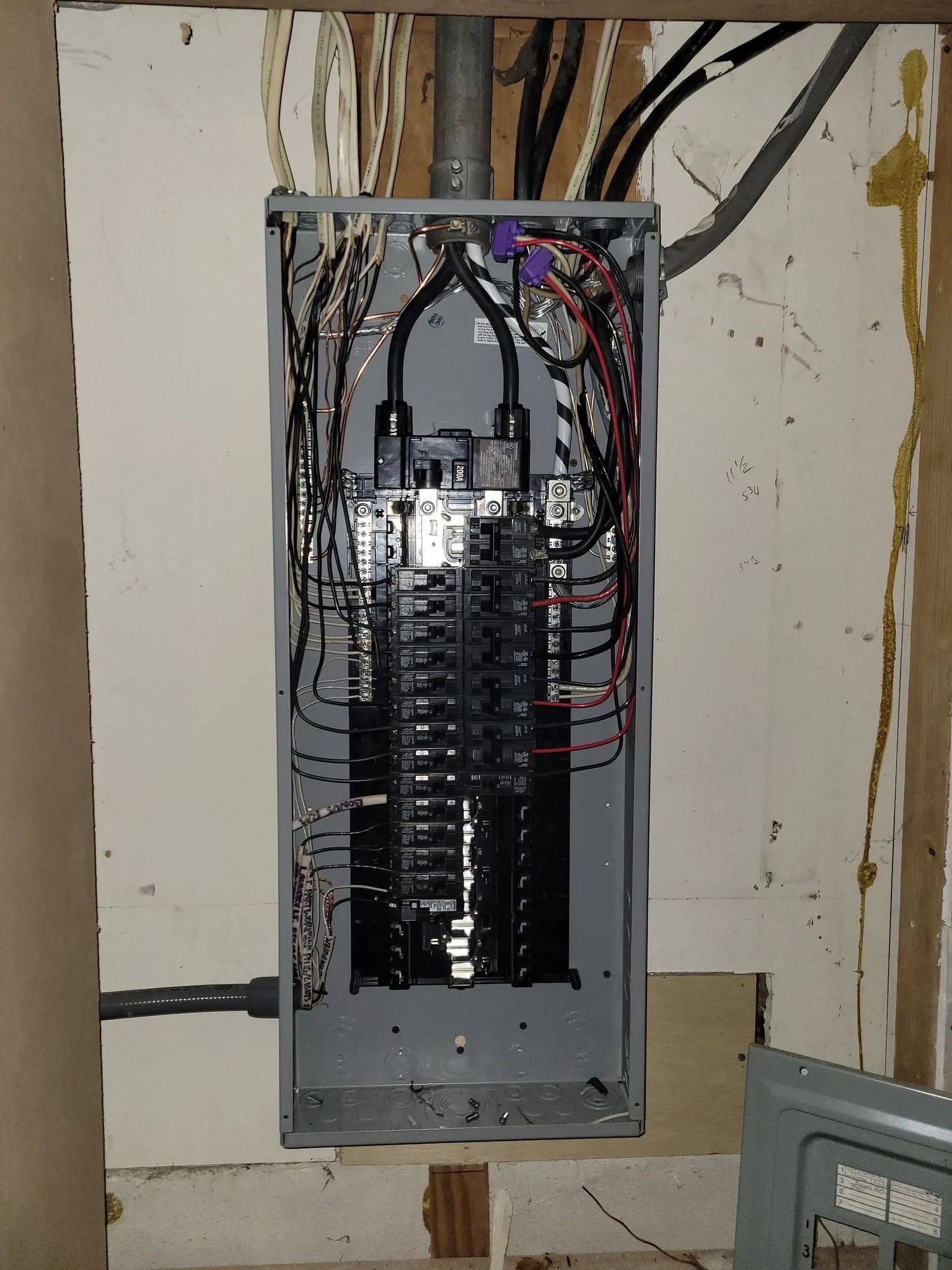 Open electrical breaker panel with exposed wiring in a wall recess.