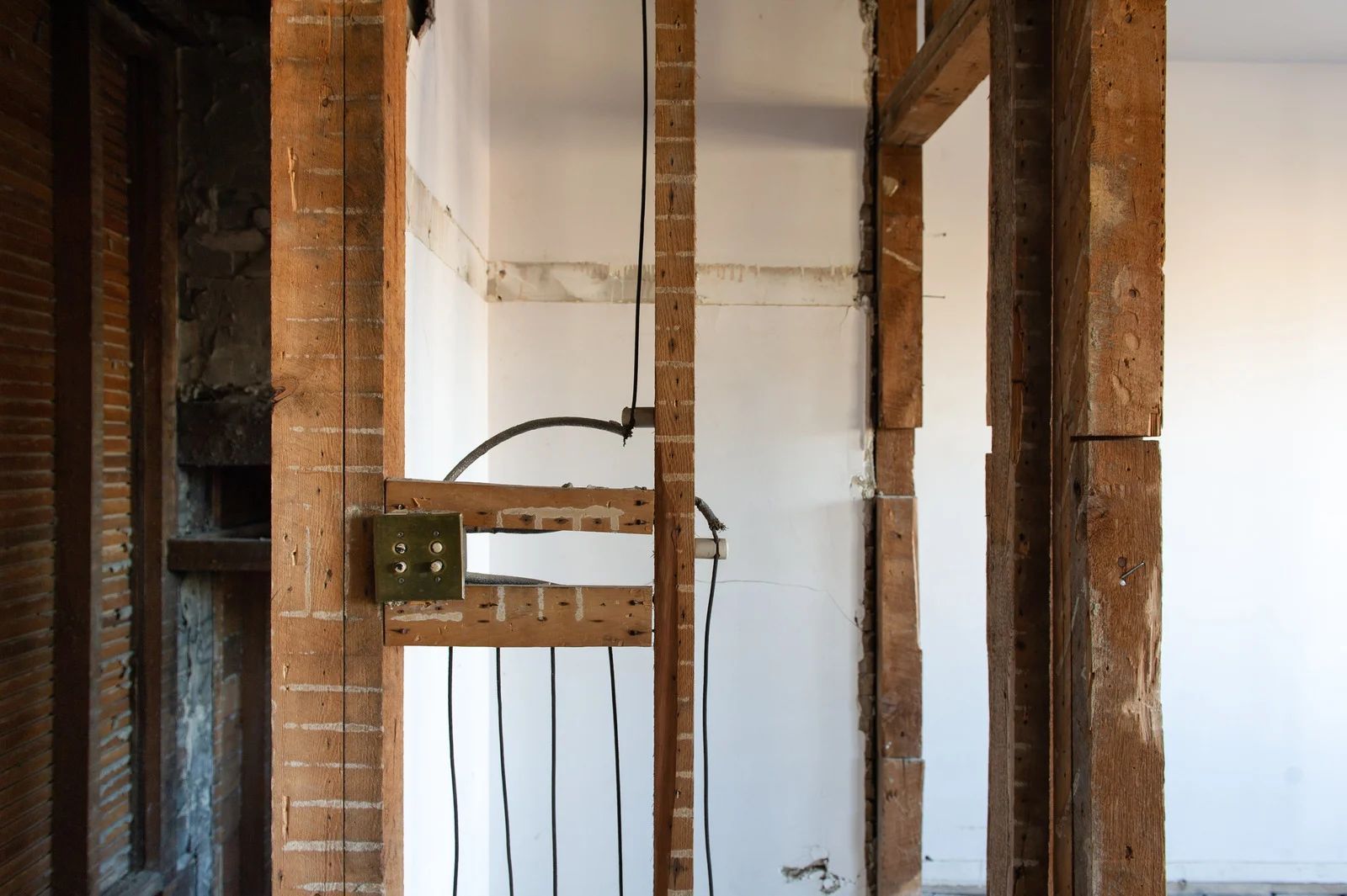 Exposed wall framing in a room under renovation, with brick studs and white plaster walls.