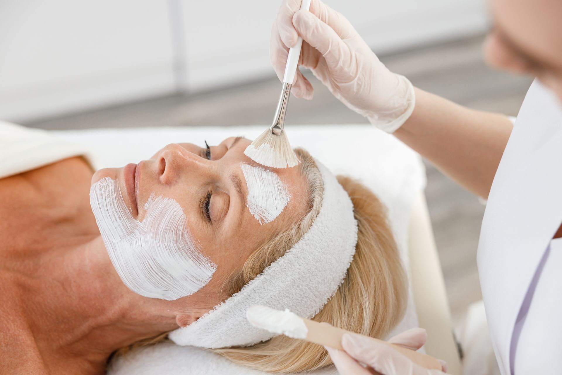 Spa facial treatment with esthetician applying mask to a client lying down