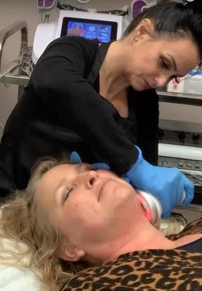Technician in blue gloves treats a reclining patient with a facial device in a clinic room
