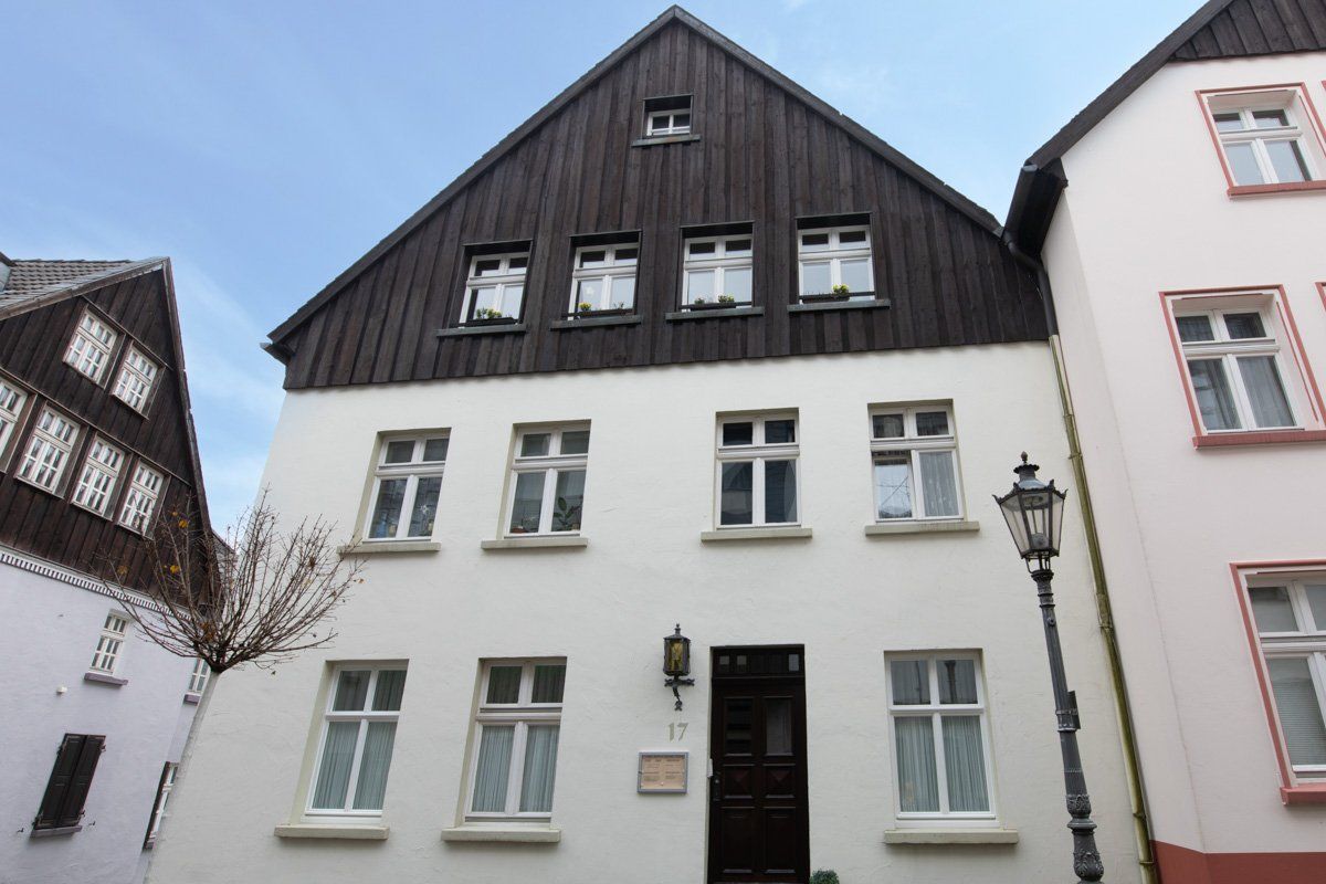 Ein weißes Gebäude mit einem braunen Dach steht neben einem rosa Gebäude