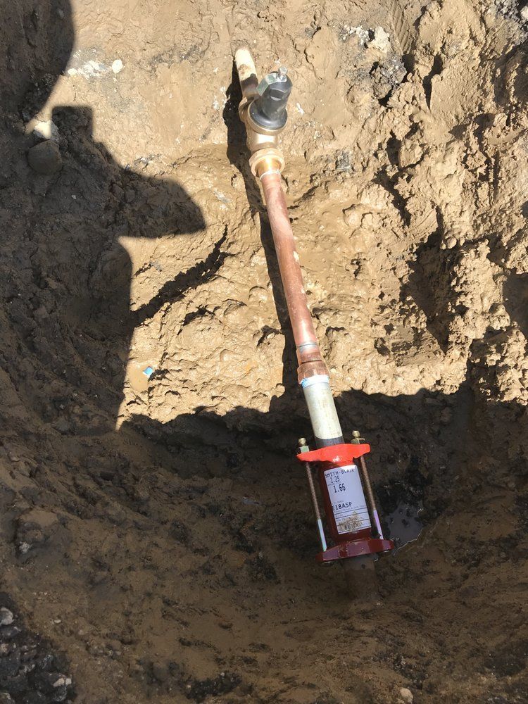 A copper pipe is laying in the dirt in a hole.