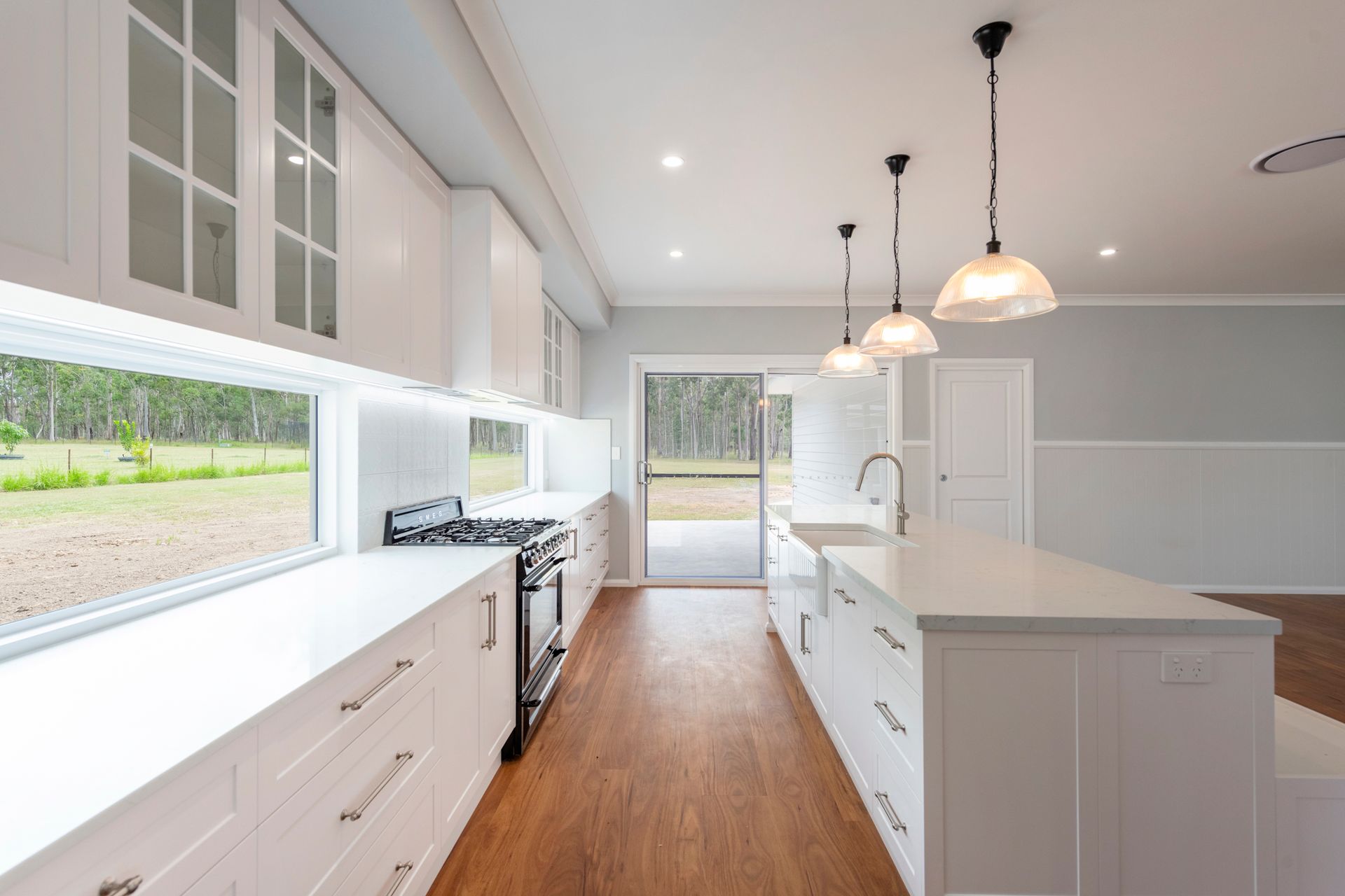 White kitchen with long island, cabinets, and cooktop, with large windows and a door to the outside.