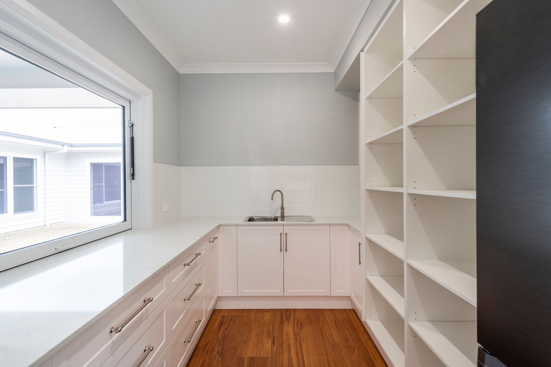 Pantry with white cabinets, open shelving, sink, and window with an outside view.