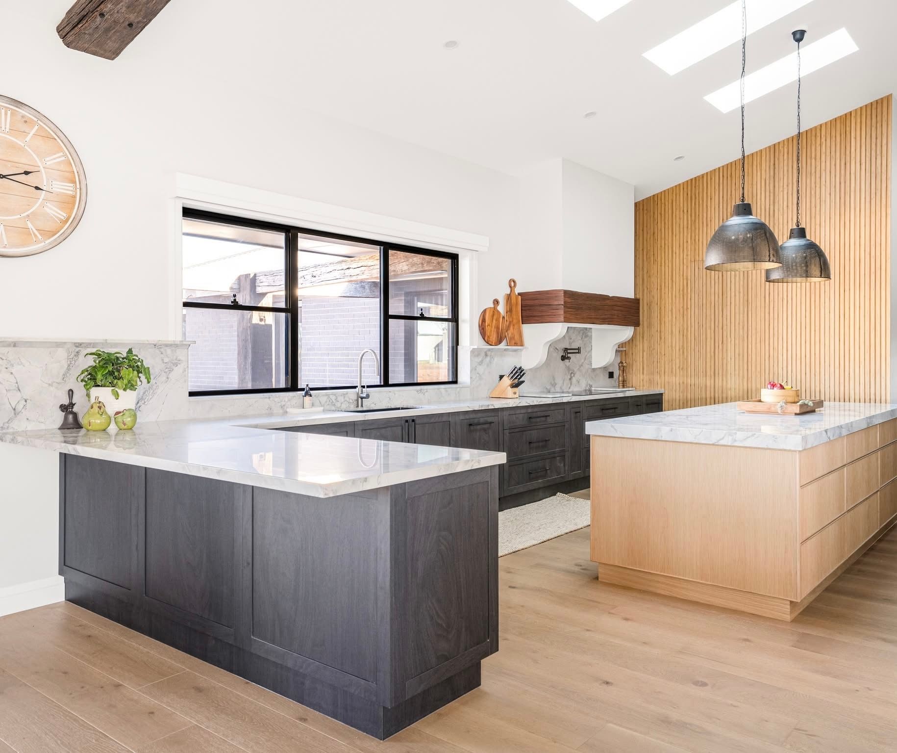 Modern kitchen with gray and wooden islands, white countertops, wood paneling, and pendant lights.