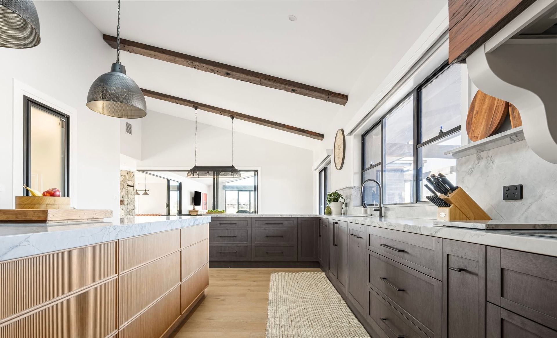 Modern kitchen with dark cabinets, wooden beams, and large windows.