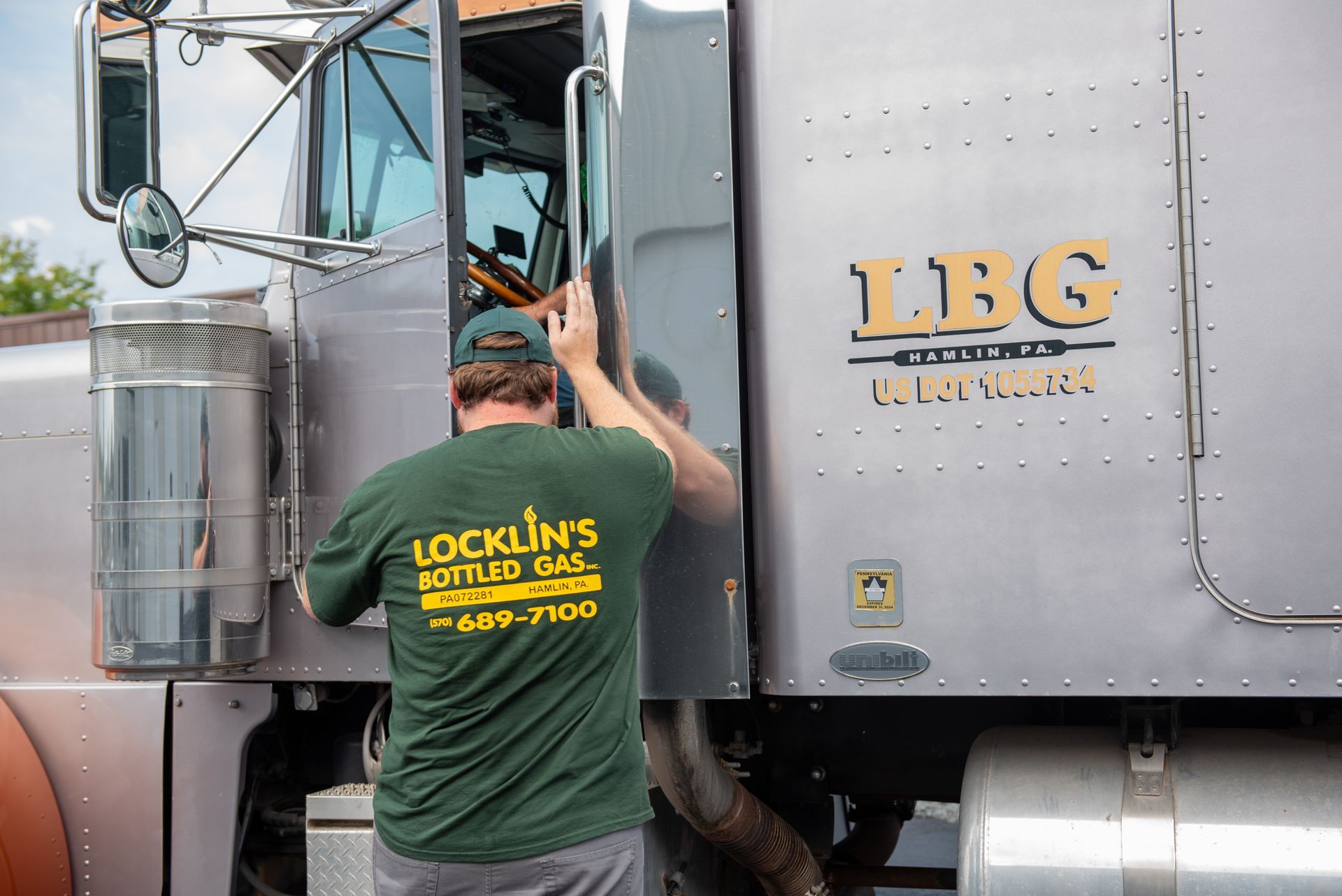 A man in a green shirt is opening the door of a semi truck.