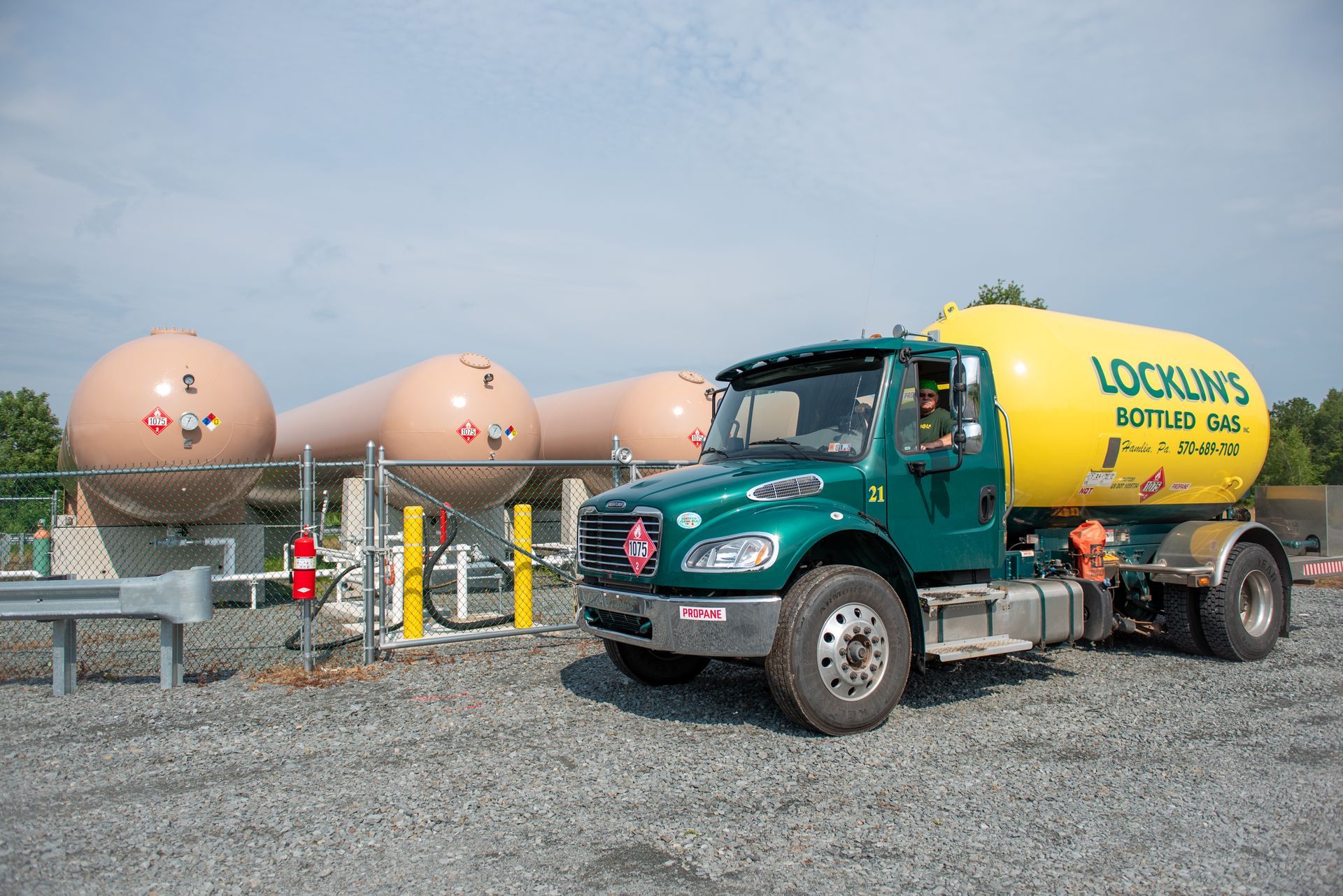 A green and yellow tanker truck is parked in a gravel lot.
