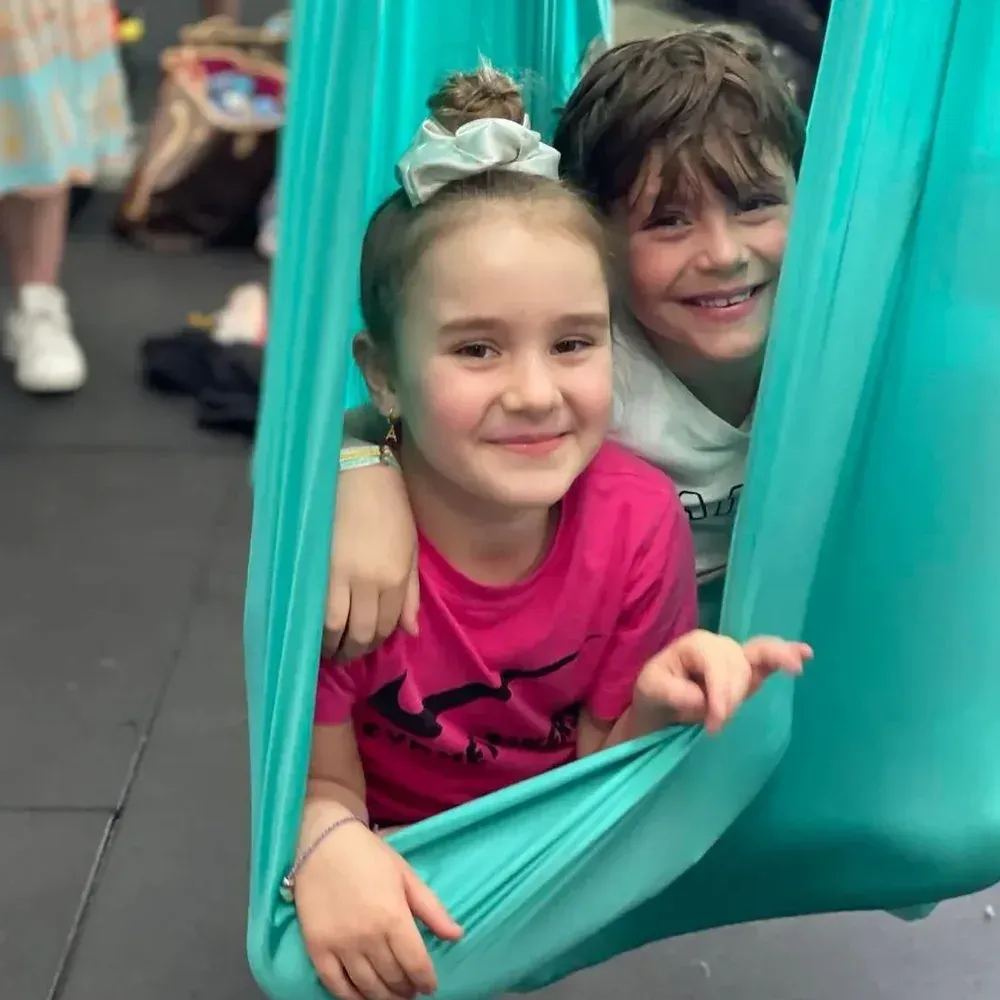 A boy and a girl are sitting in a hammock.