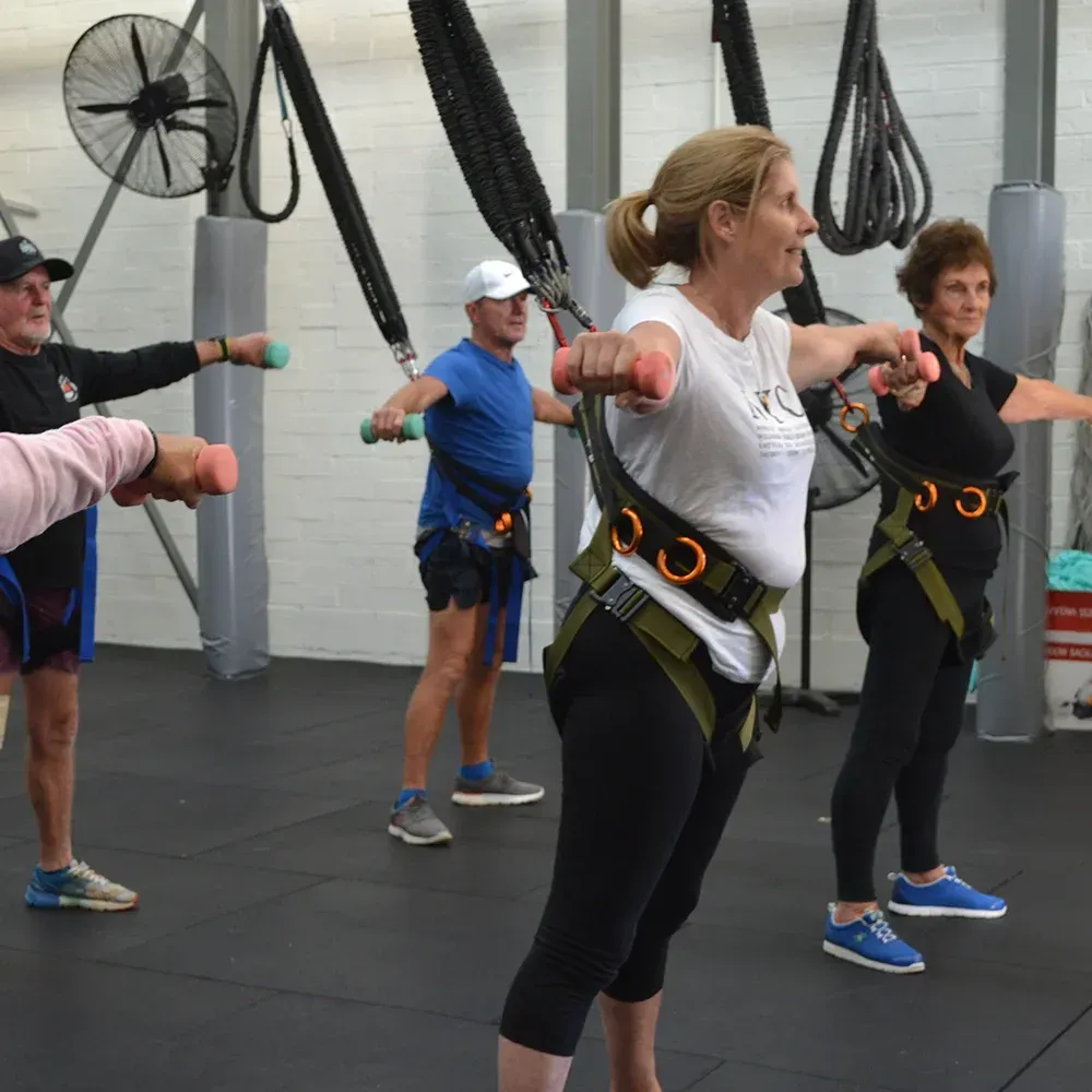 A group of people are doing exercises with dumbbells in a gym