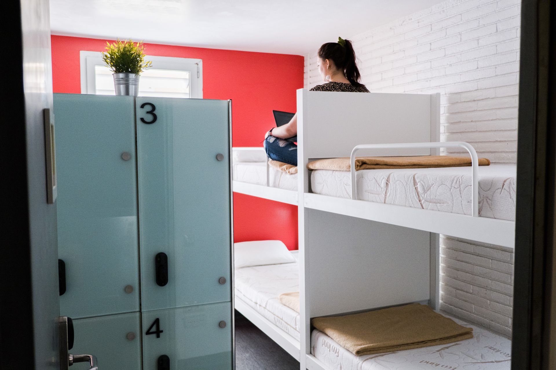 A woman is sitting on a bunk bed in a dorm room.