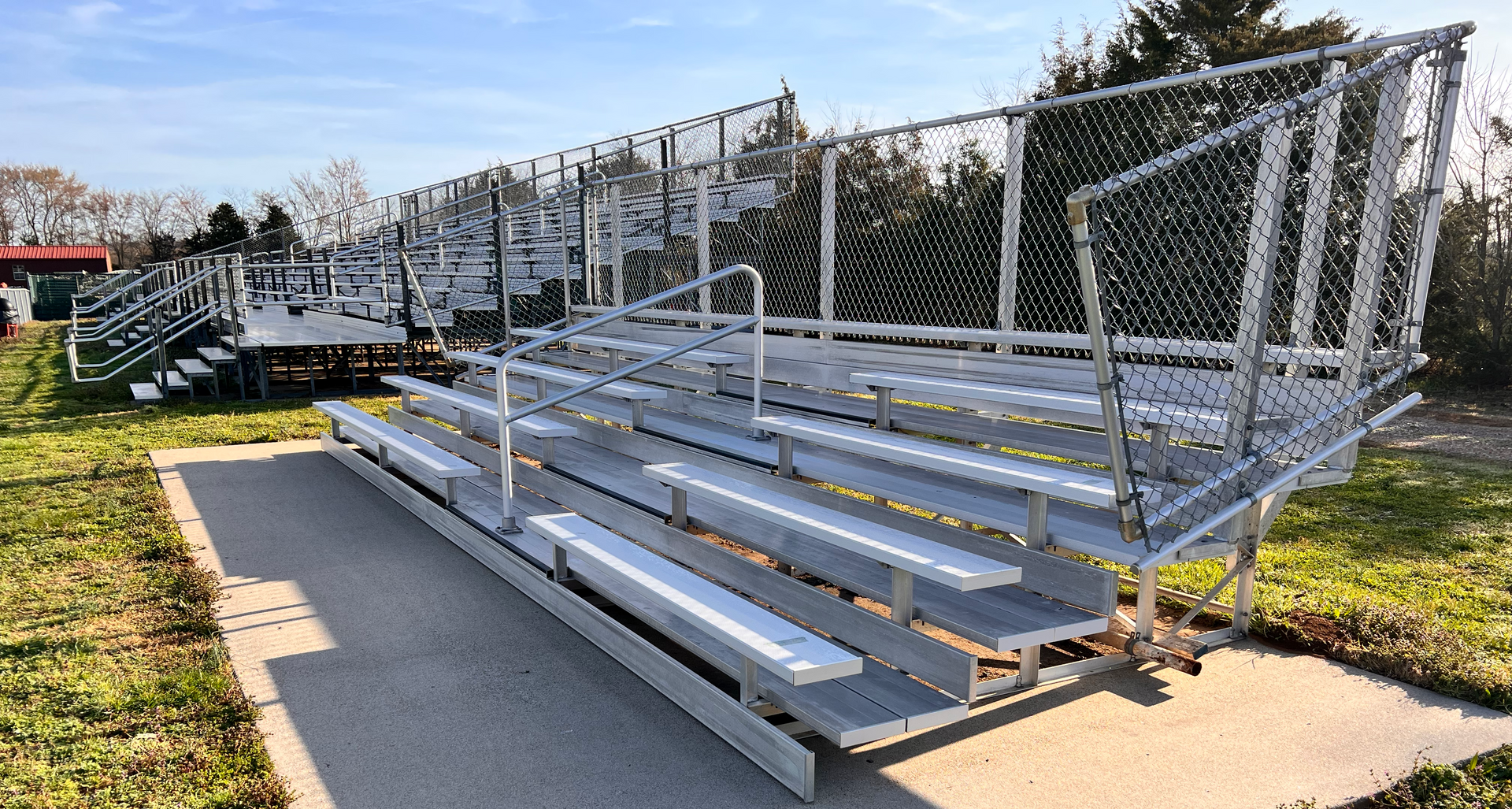 Bleachers on a concrete pad with a chain-link fence, outdoors on a sunny day.
