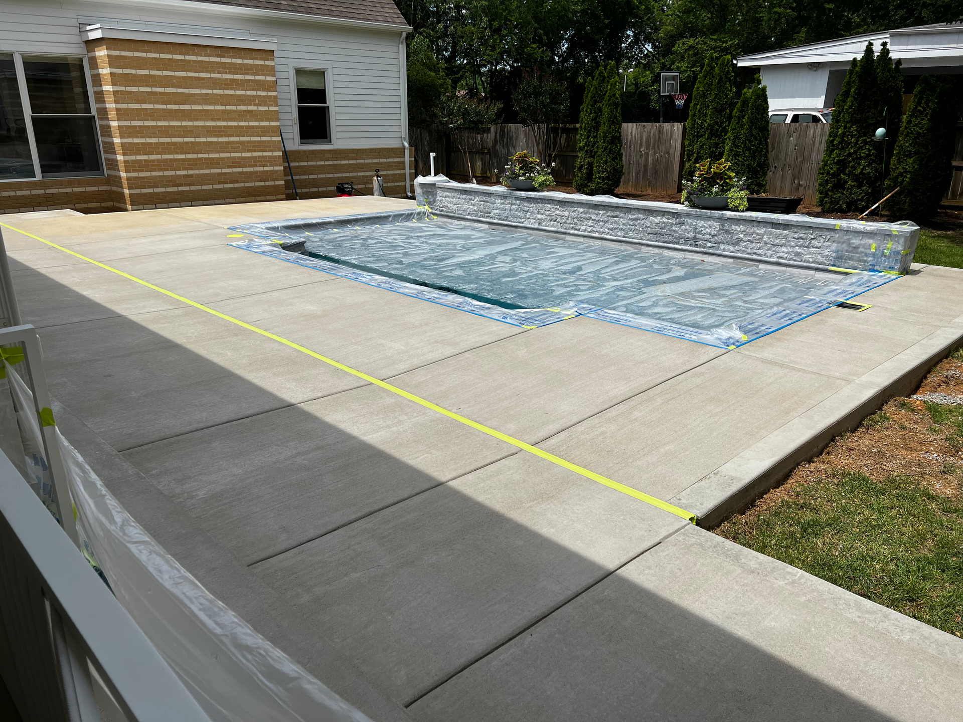 Concrete patio with pool and cover; building in background. Sunny day.