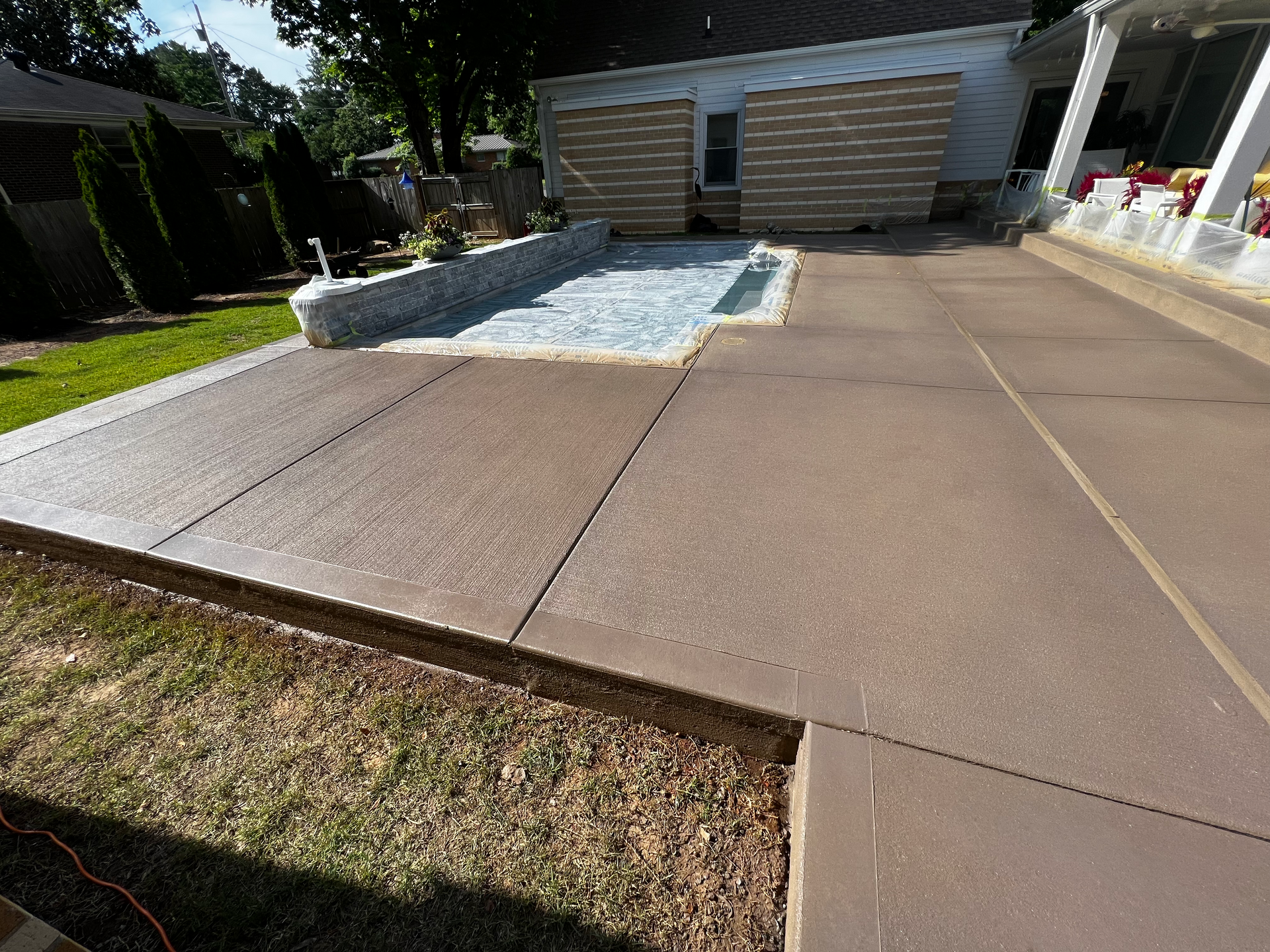 Brown concrete patio with a small gravel area, house, and green grass in the yard.