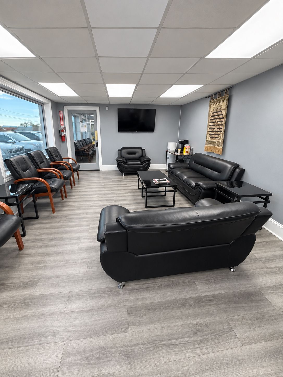 Empty office waiting room with black leather couches, chairs, a wall-mounted TV, and large windows | Yaffo Auto Service