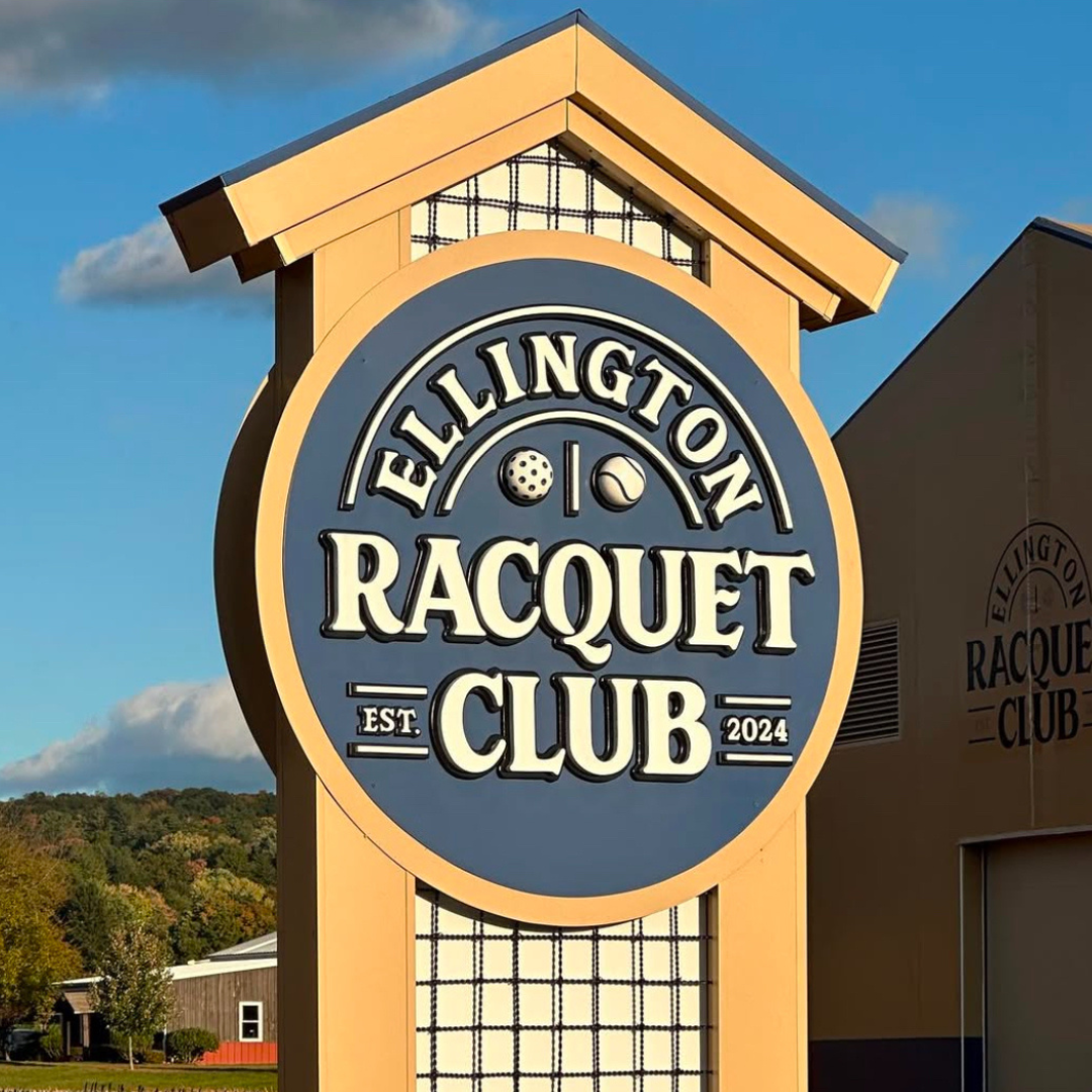 Sign for Ellington Racquet Club, blue circle with white text, on a yellow structure.