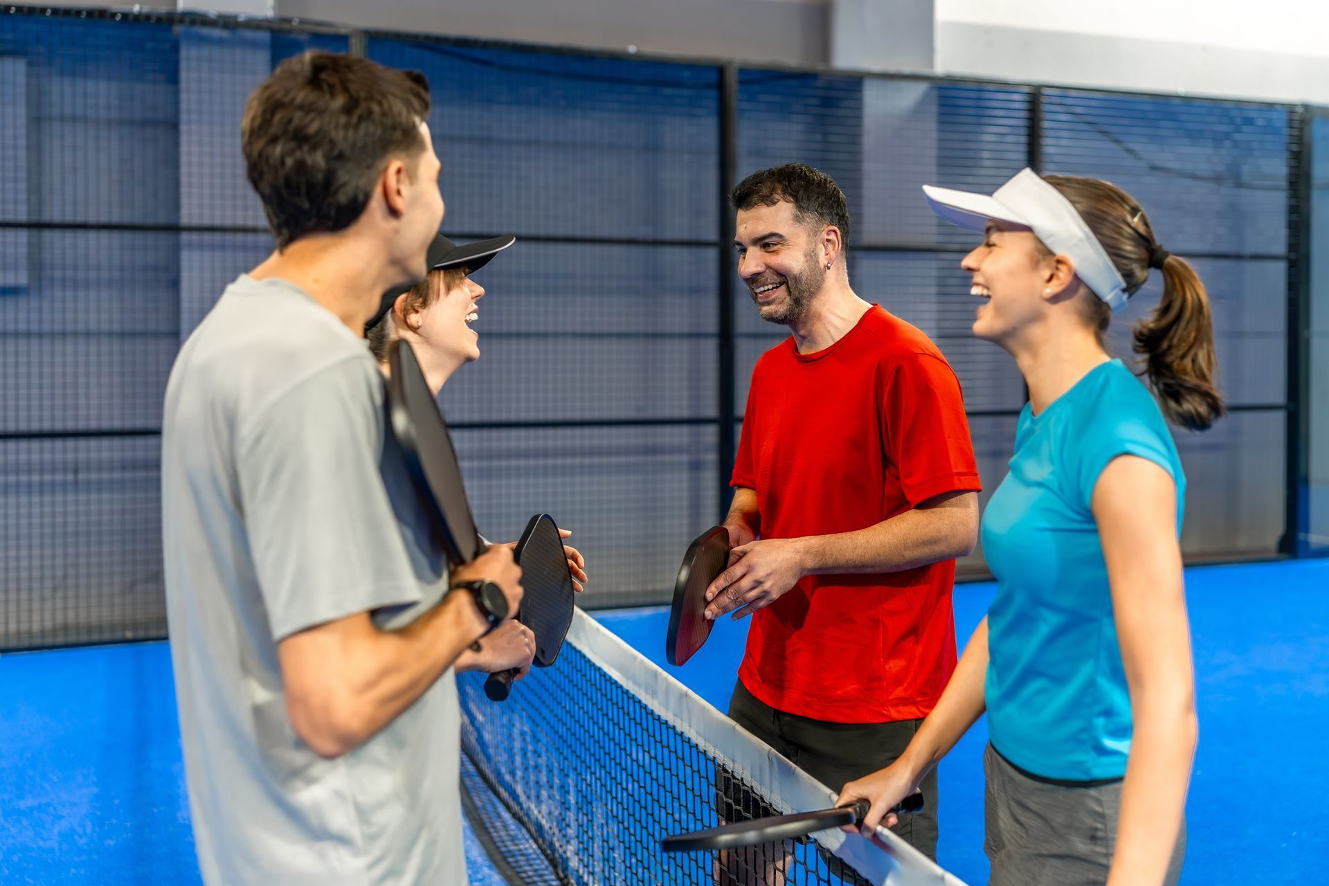 Four people talking and smiling beside a tennis net on an indoor court