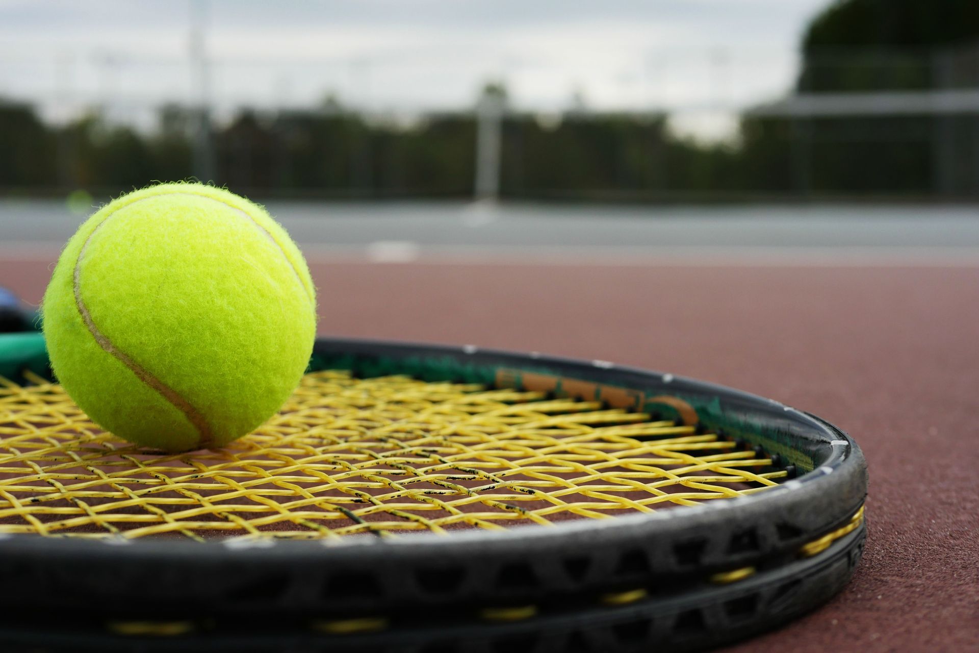 Tennis ball resting on a racket on a court, with a blurred background.