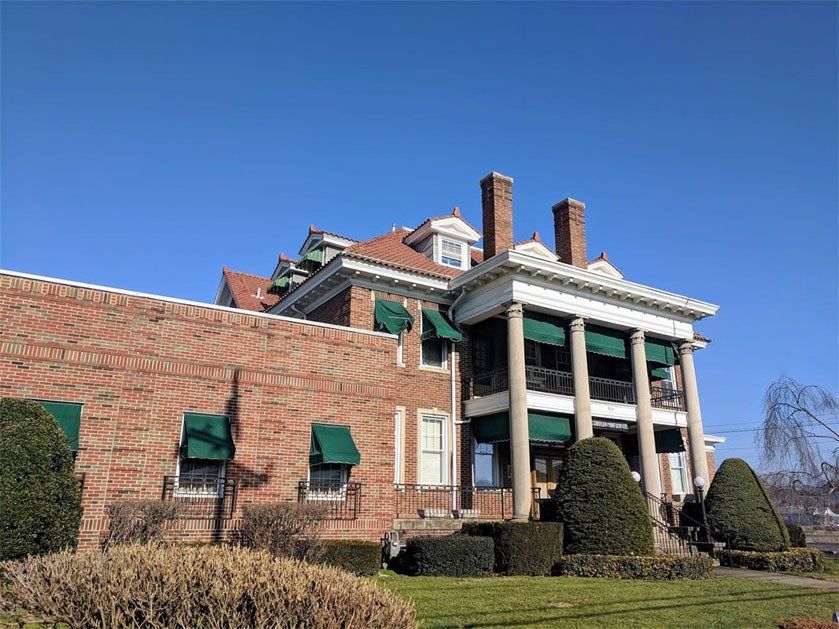 Large brick mansion with green awnings and white columns under a clear blue sky