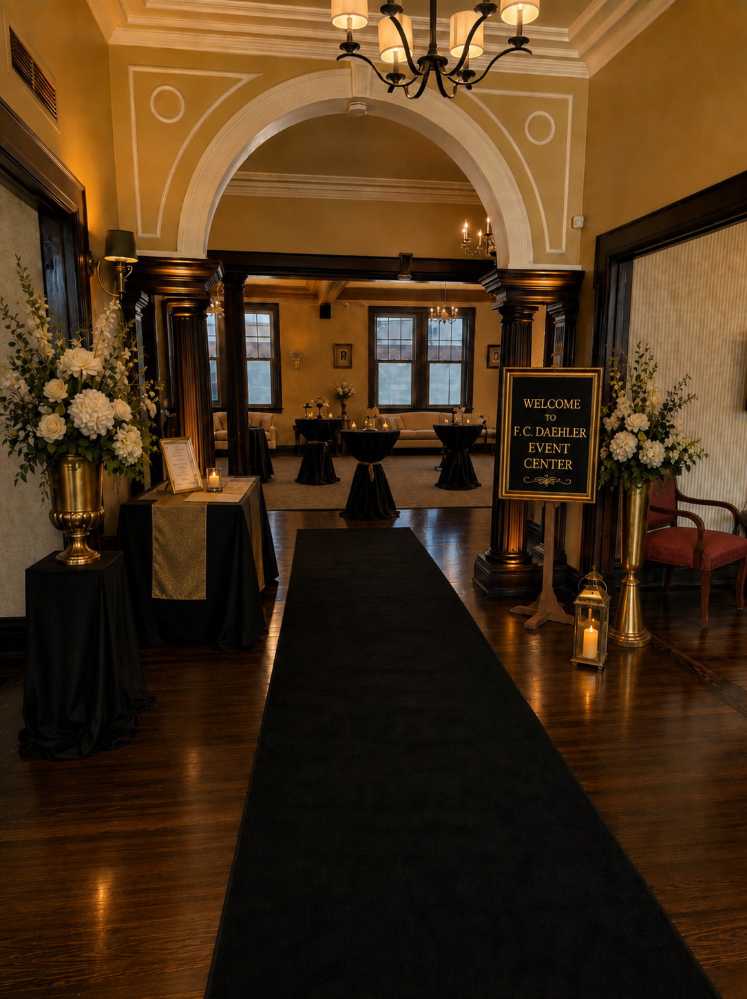 Elegant indoor aisle with black runner, floral stands, and a framed sign beneath an archway