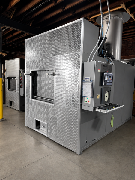 Large industrial machine with silver paneling and dark gray base in a warehouse or factory.