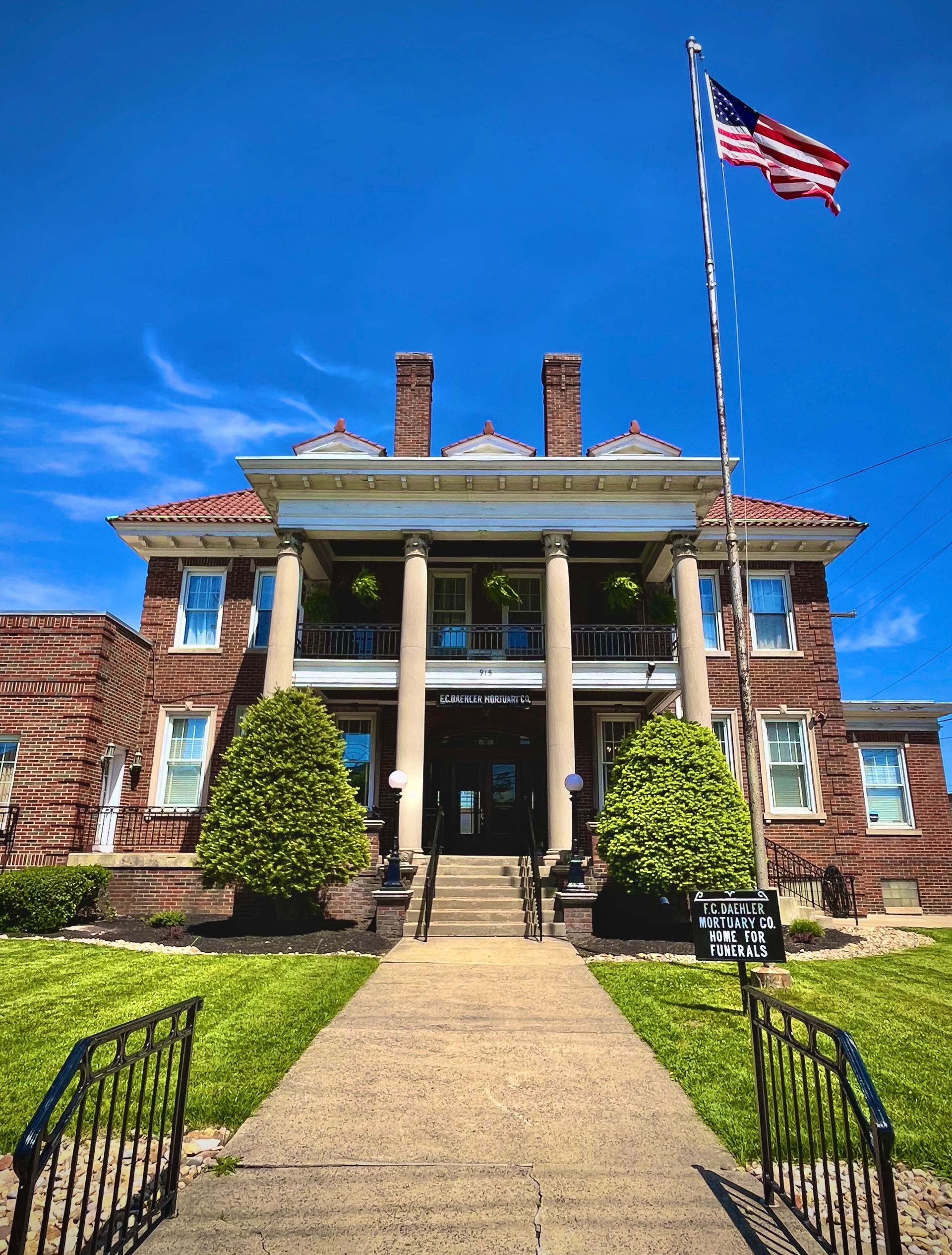 Historic brick mansion with white columns and an American flag flying on a sunny day