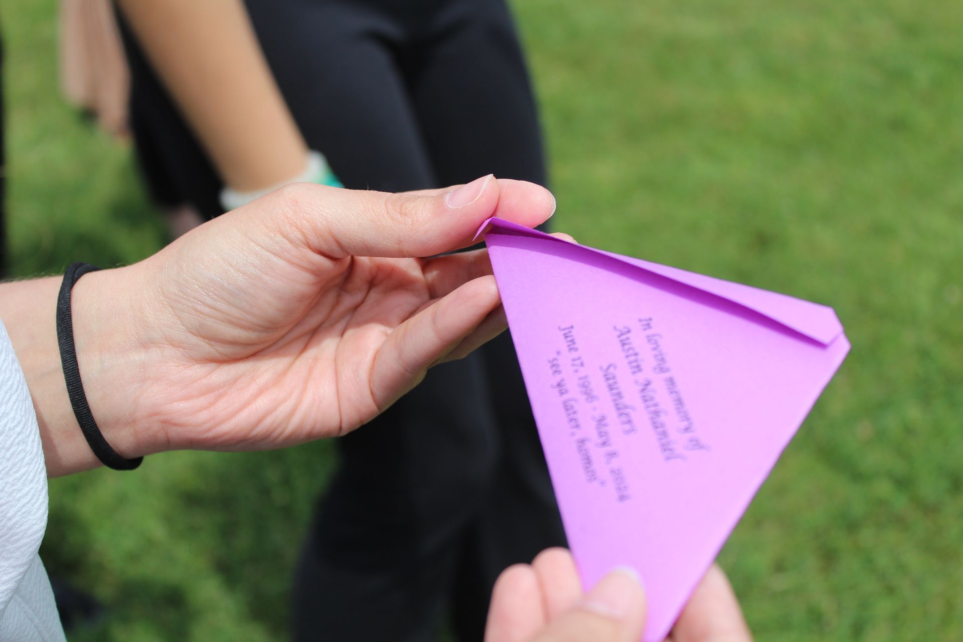 Hands holding a folded purple paper note outdoors on grass