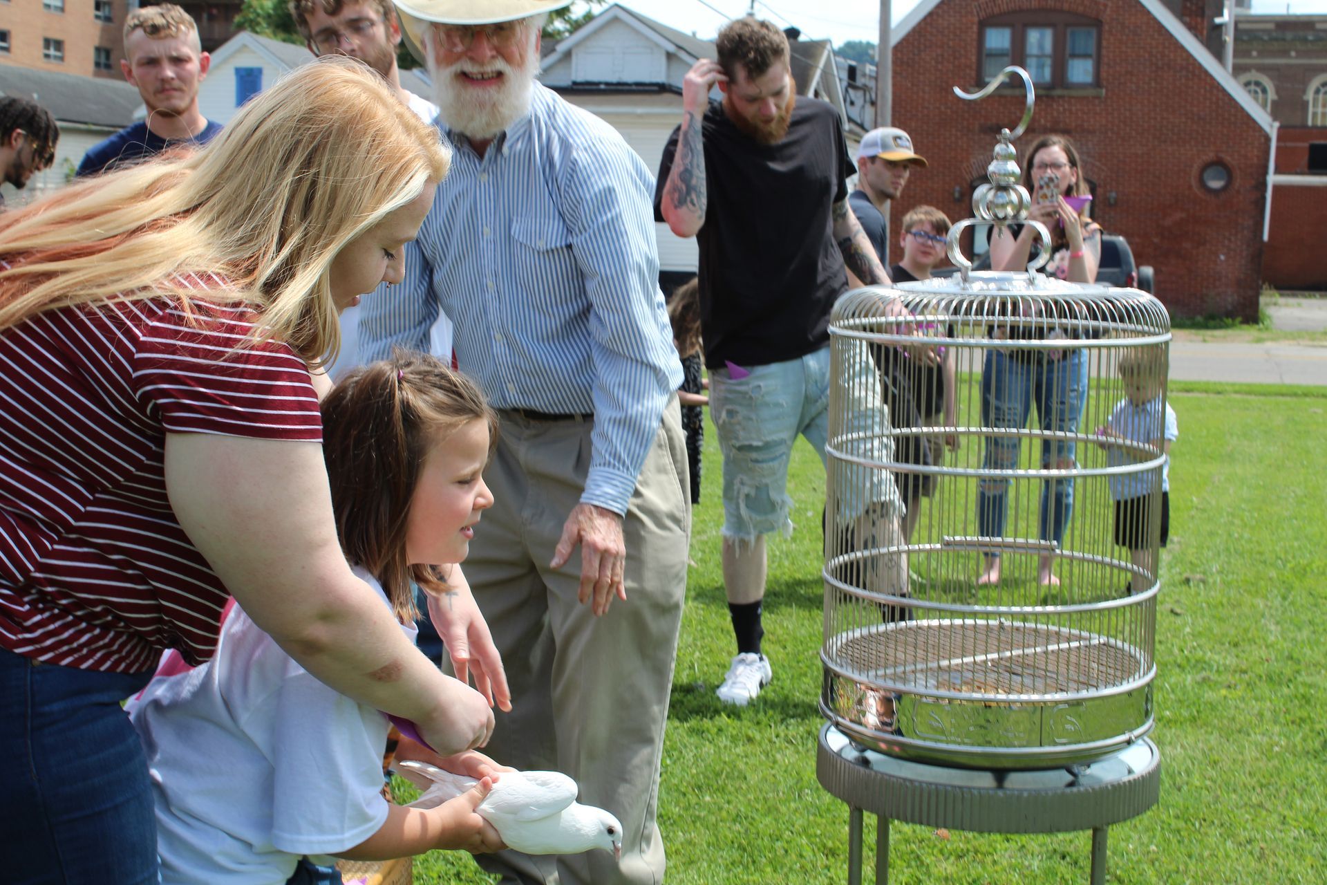 Children and adults watch a wire cage on stands in a grassy yard at an outdoor event