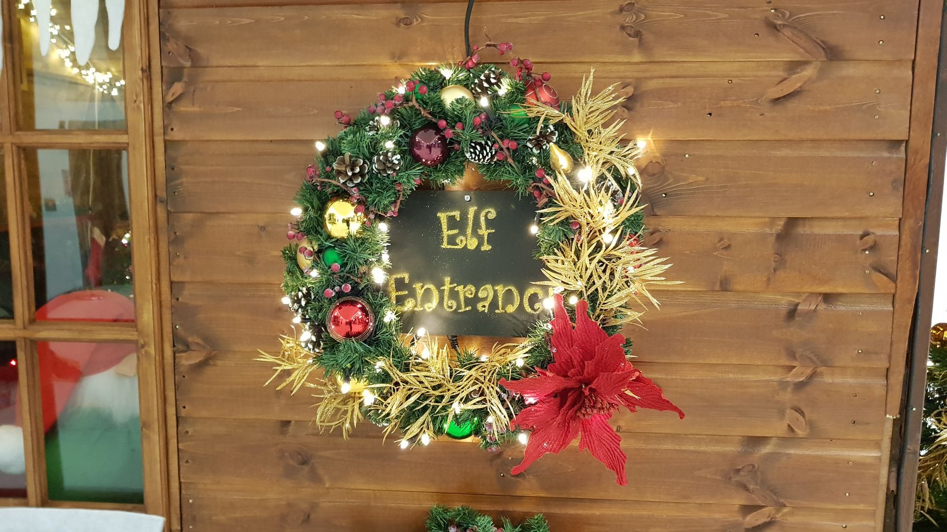 A christmas wreath is hanging on a wooden wall.