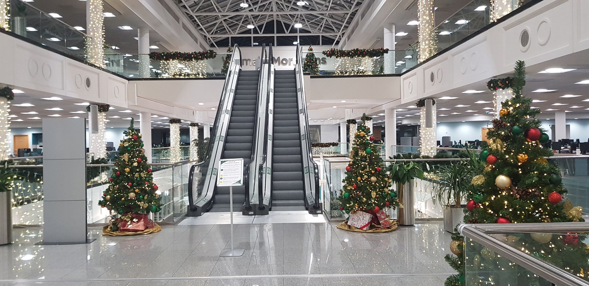 A shopping mall decorated for christmas with christmas trees and an escalator.