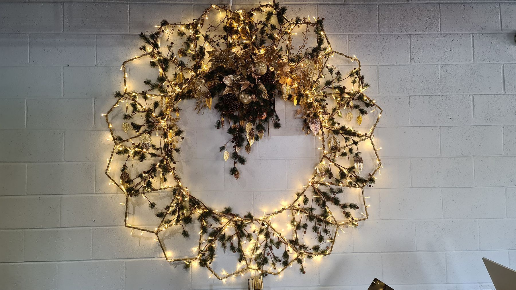 A wreath with lights on it is hanging on a white brick wall.