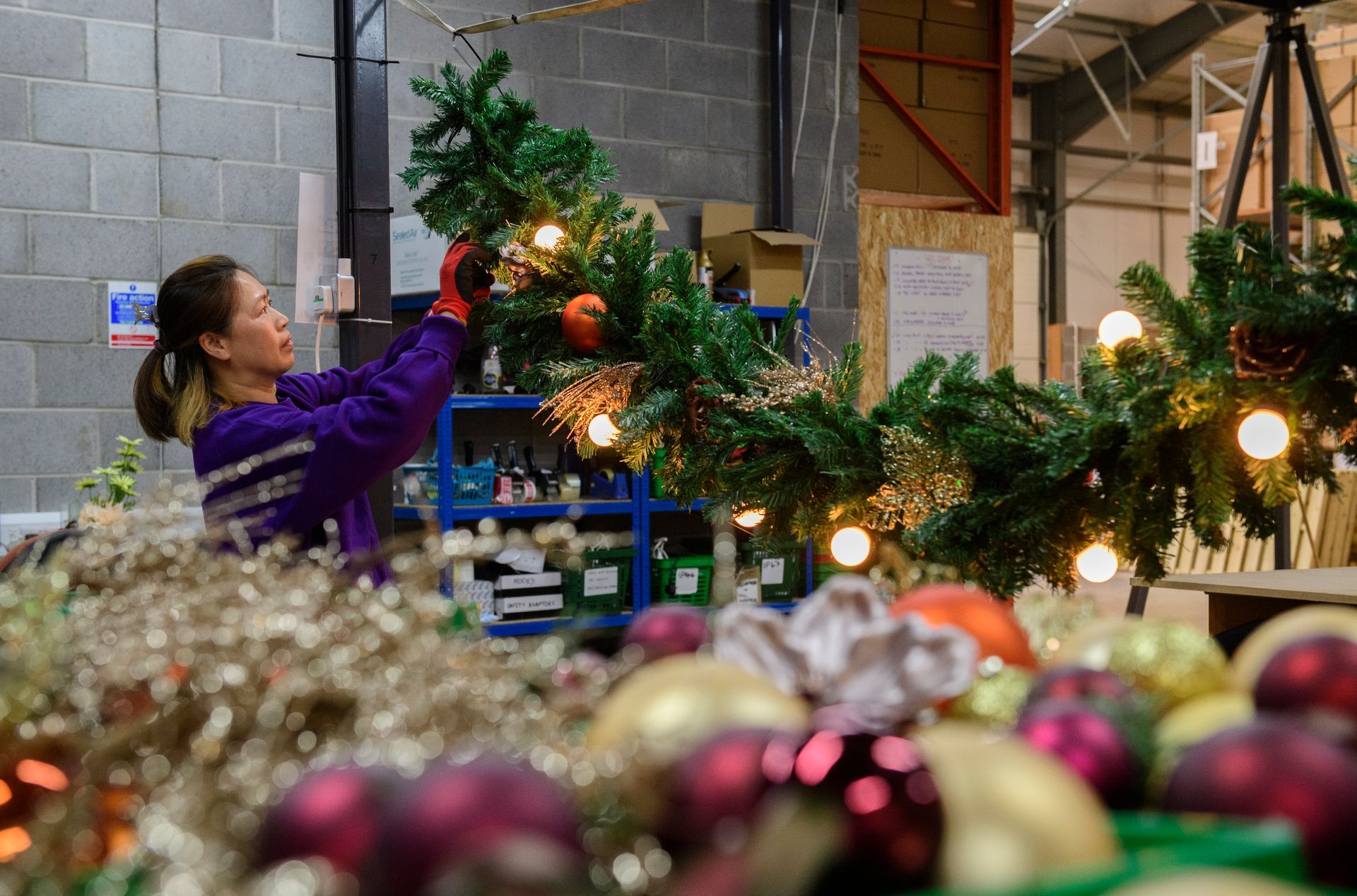 Person decorating a Christmas tree in a produce market with apples in the foreground